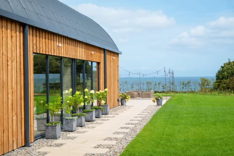 A side view image of the Anglesey Barn showing patio area, green space and views out to sea